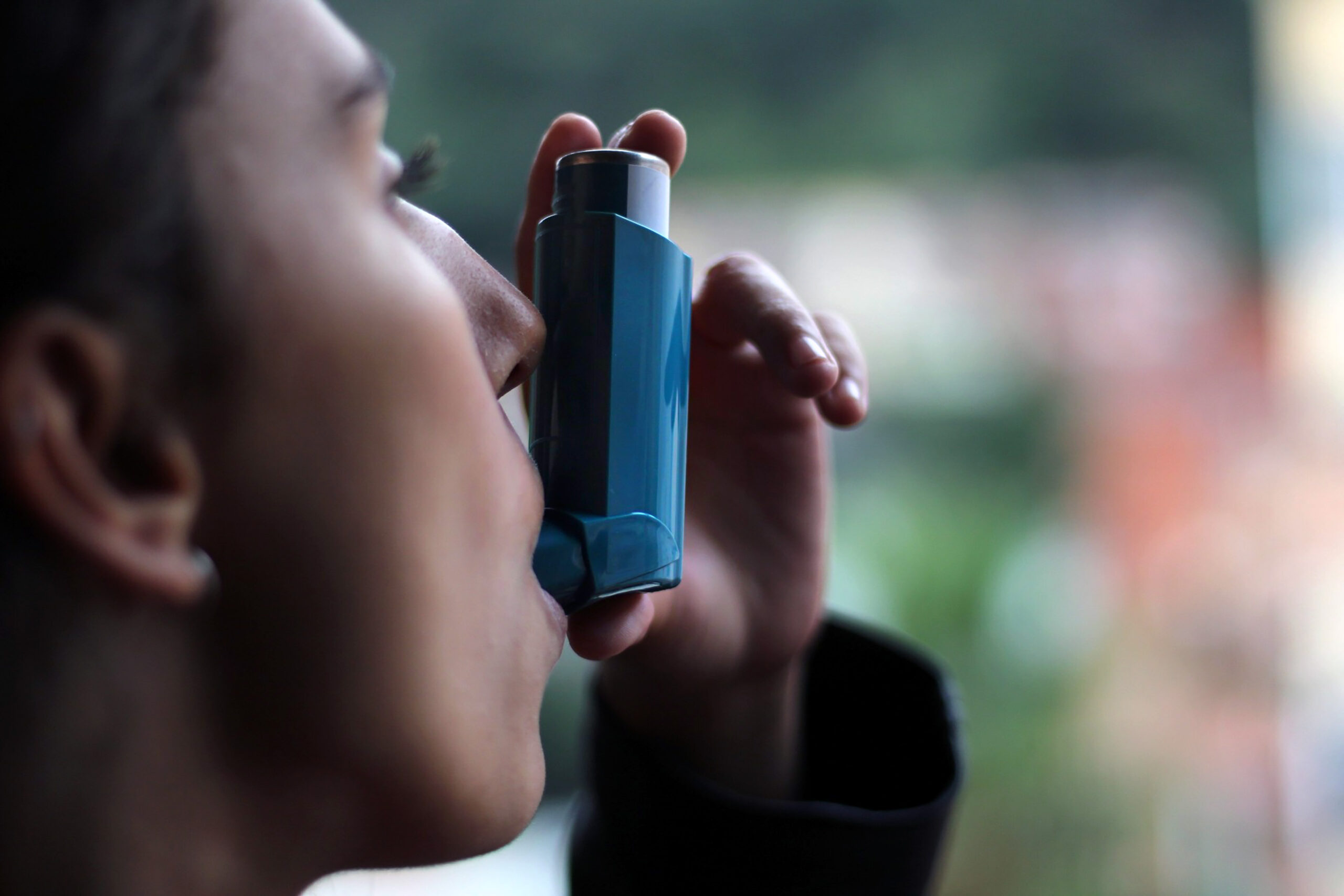 Young girl using blue asthma inhaler to prevent an asthma attack.