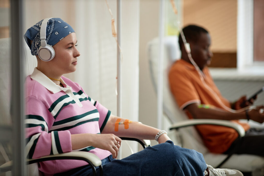Side view portrait of two people getting chemotherapy treatment in clinic while sitting in chairs with IV drip tubes.