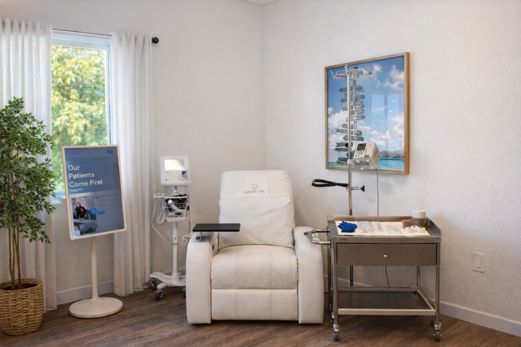 A single infusion chair sits in a room next to an IV, a table, and a sign that says "Our Patients Come First".