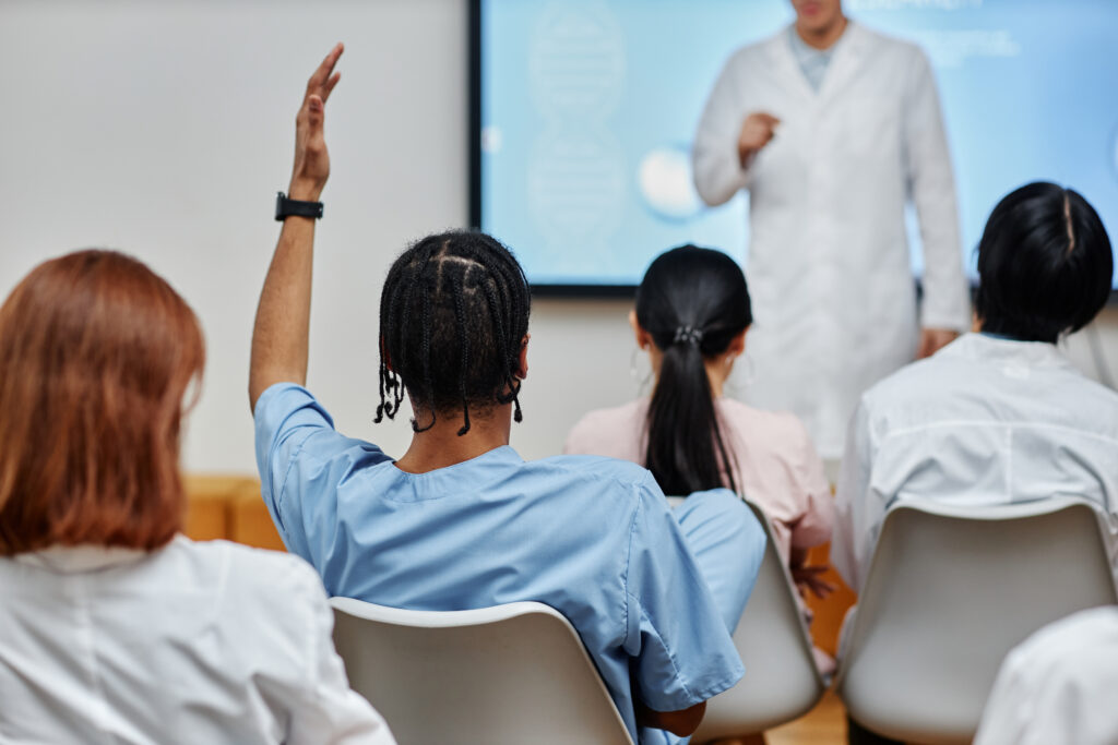 Back view of young male nurse raising hand in class at a medical seminar.