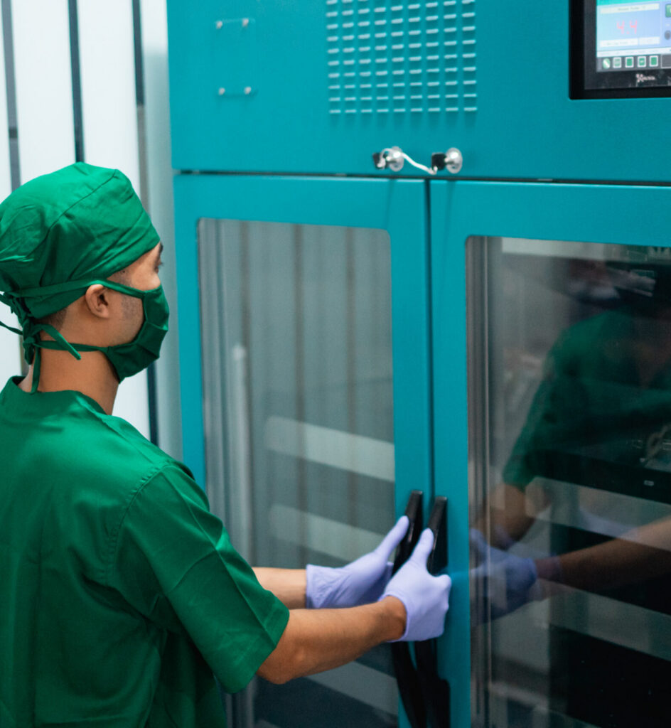 Doctor in uniform wearing a mask and rubber gloves holds the handle of the IV storage fridge.